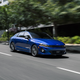A blue sedan warps the fabric of space and time on a business park road.
